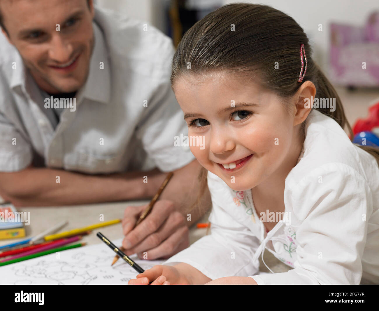 Father and daughter (3-4) colouring in book on floor, (portrait) Stock Photo