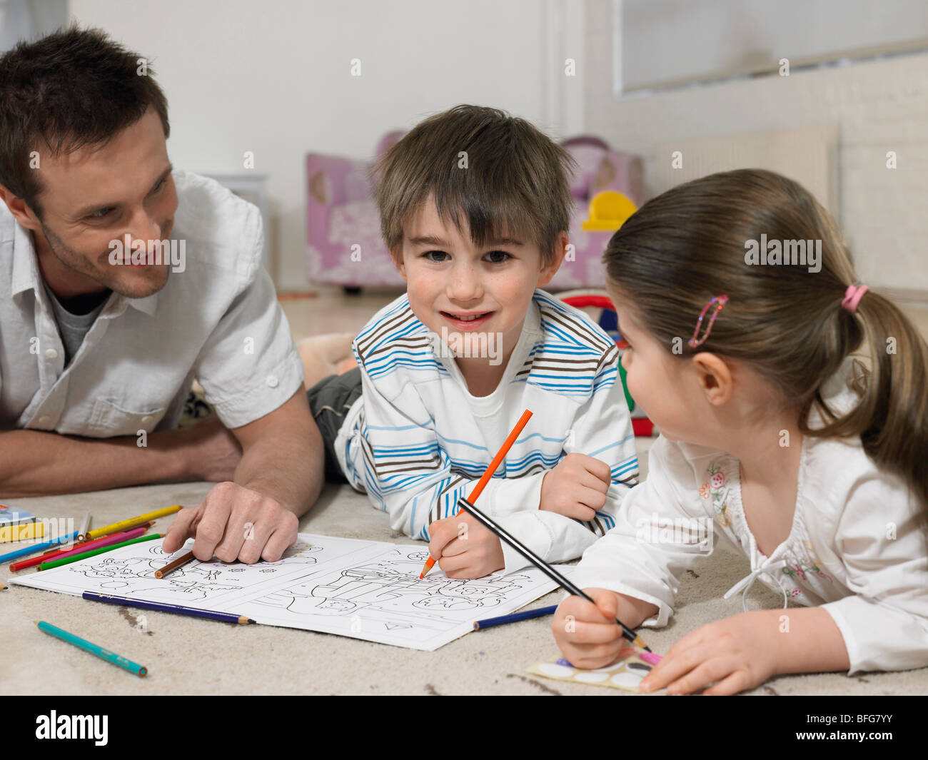 Father and Children (3-6) colouring in book on floor, (portrait) Stock Photo