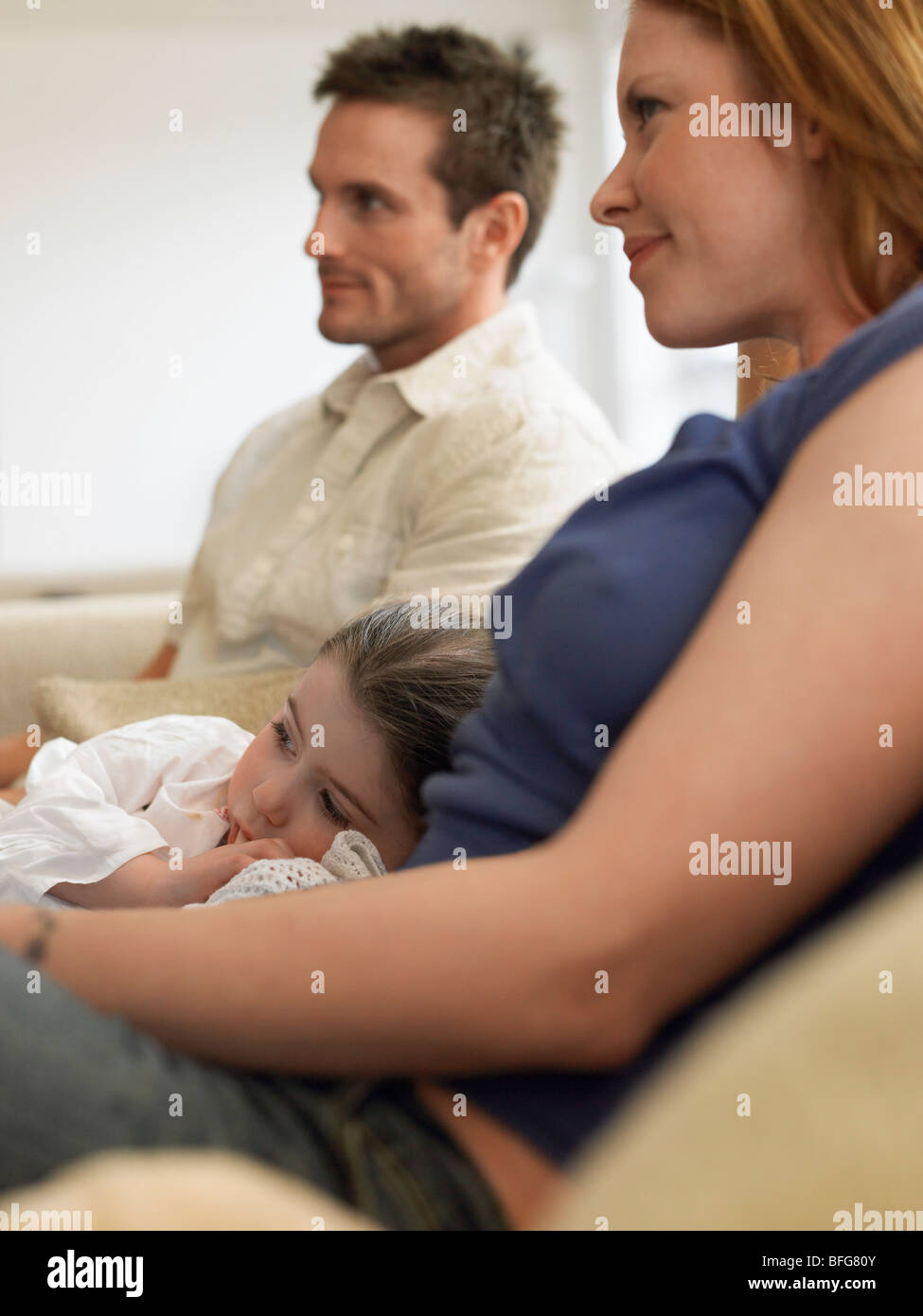 Girl (3-4) watching television with parents on couch Stock Photo
