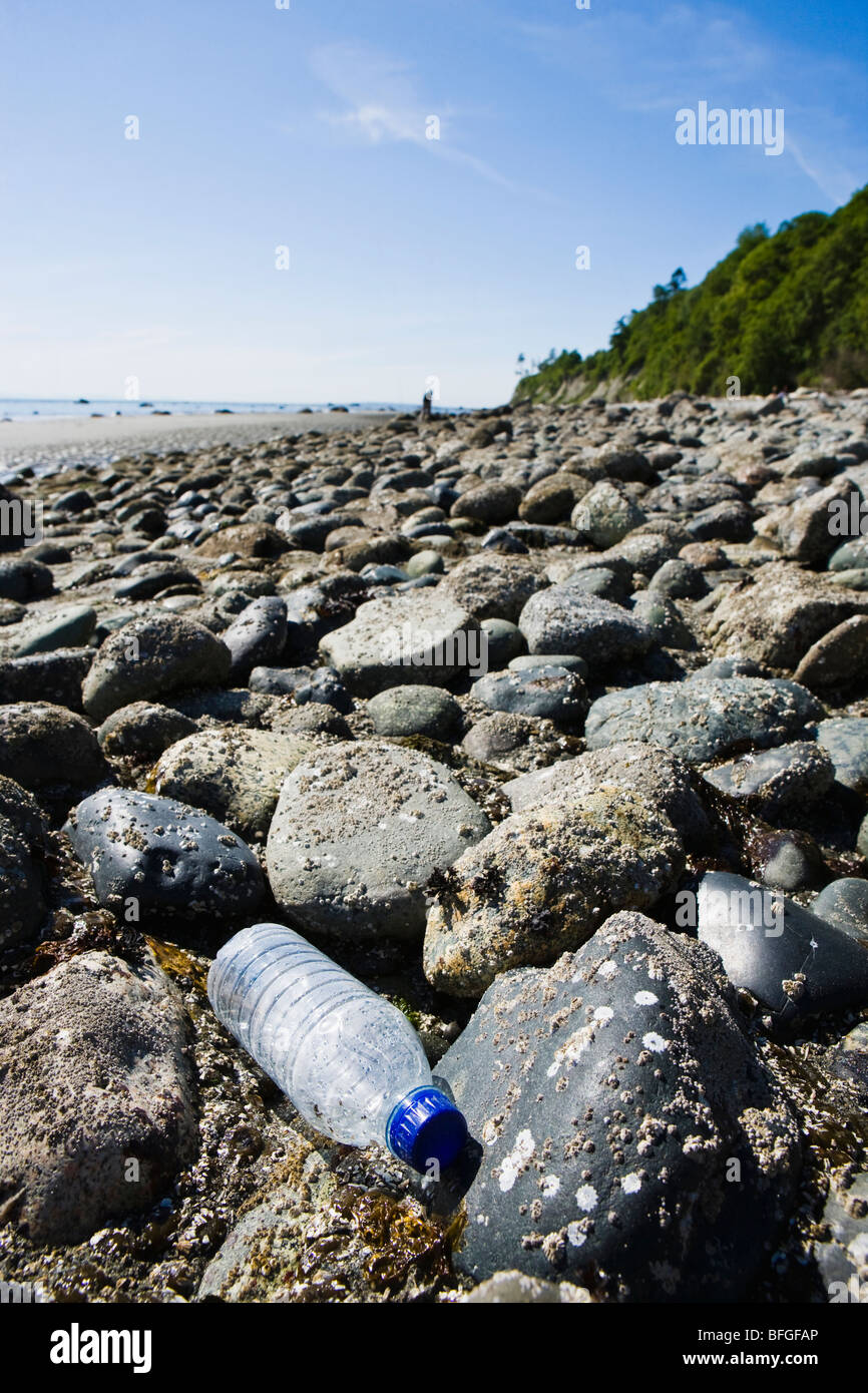 A single use clear plastic water bottle discarded on a rocky shoreline. Stock Photo