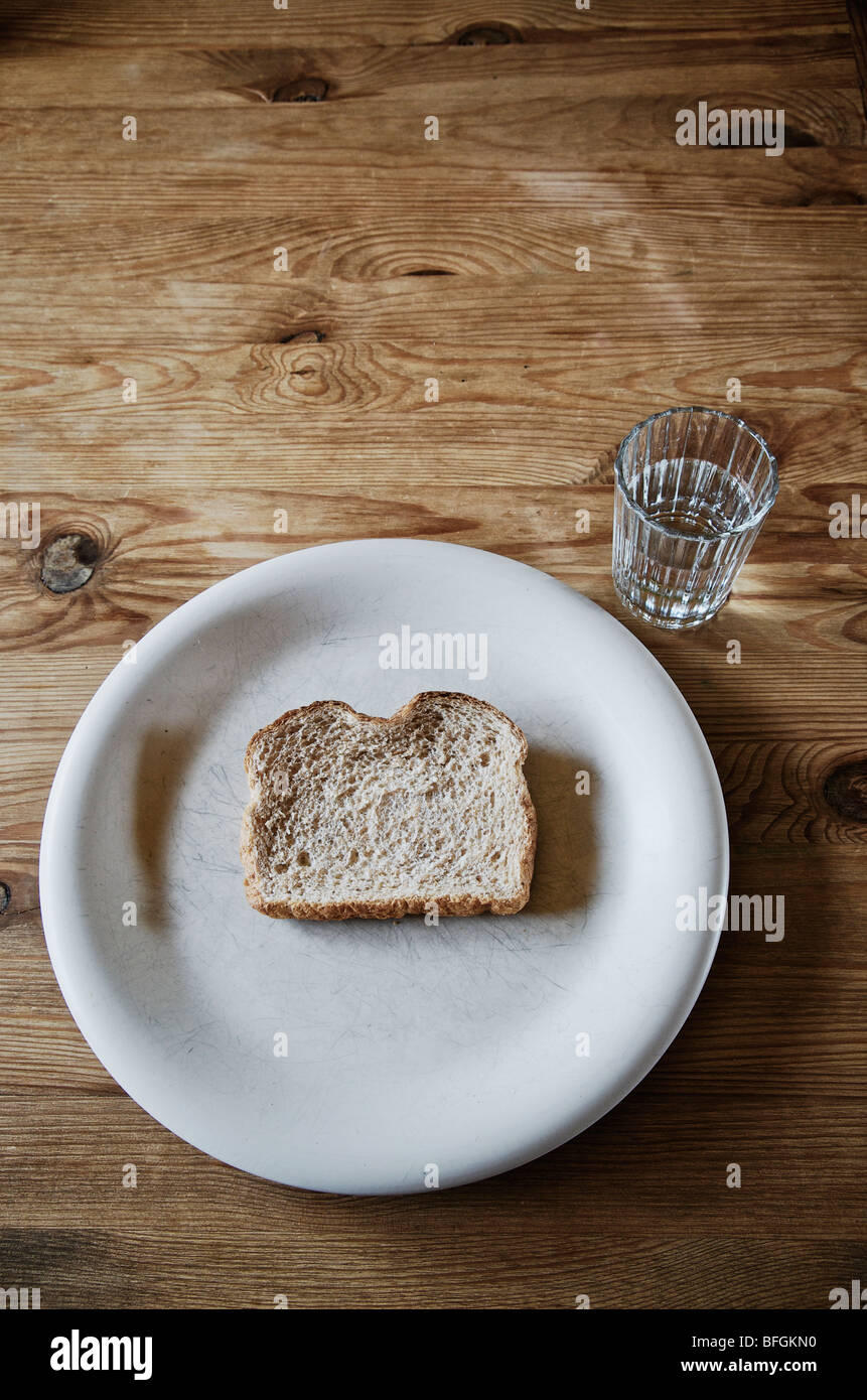 Slice of stale bread on a white plate with a glass of water Stock Photo
