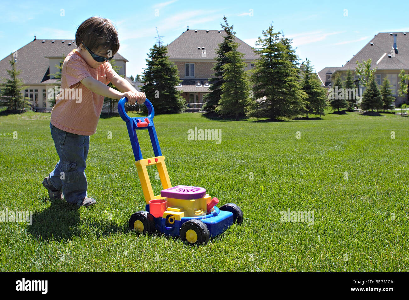Young boy mowing lawn with toy mower, King City, Ontario Stock Photo