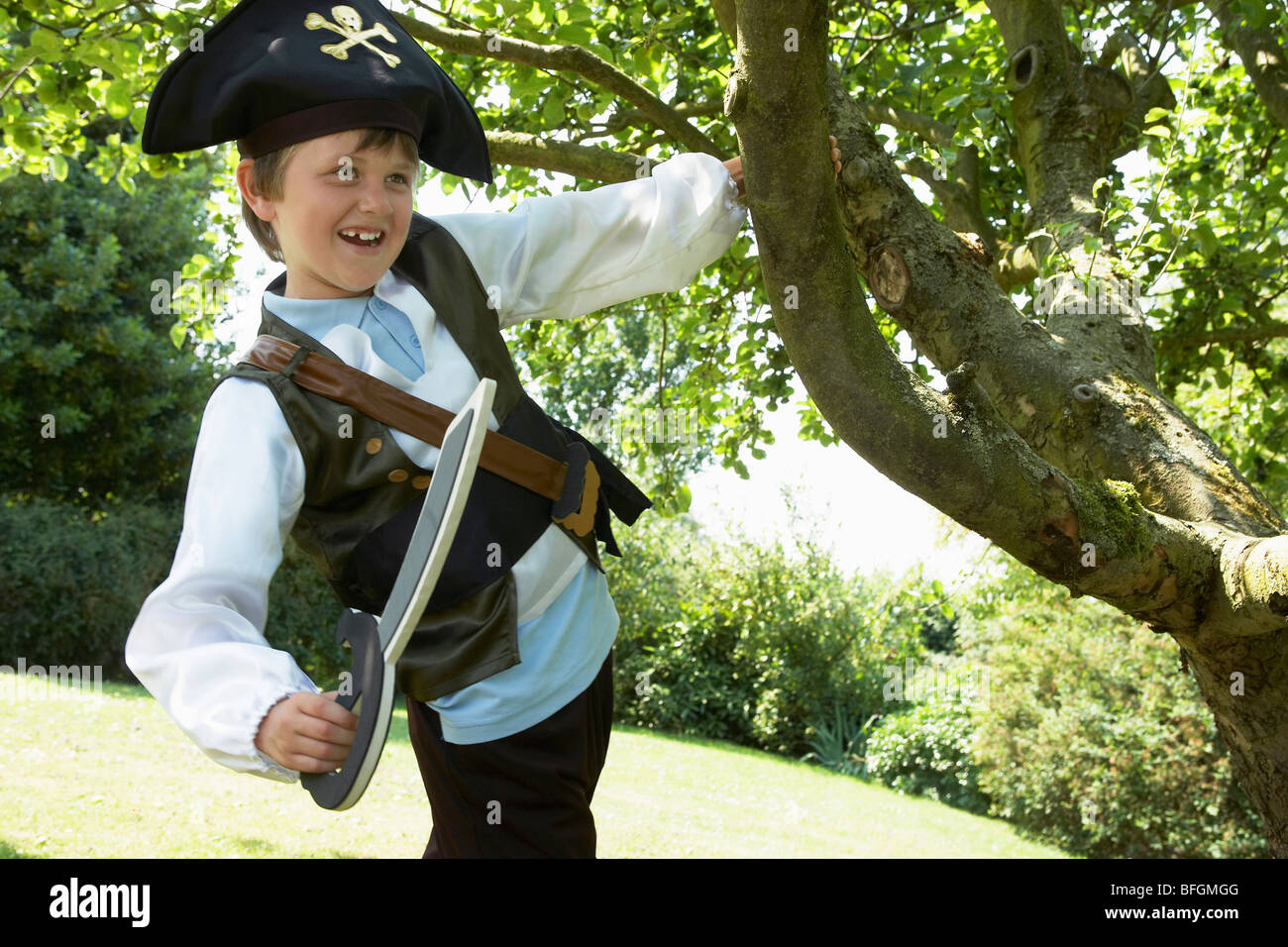 Boy Wearing Pirate Costume swinging from tree in park Stock Photo