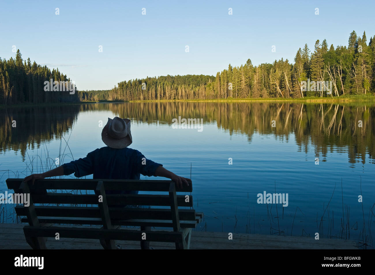 Man relaxing on park bench with a lake view. Two Mile Lake, Duck Mountain Provincial Park, Manitoba, Canada Stock Photo