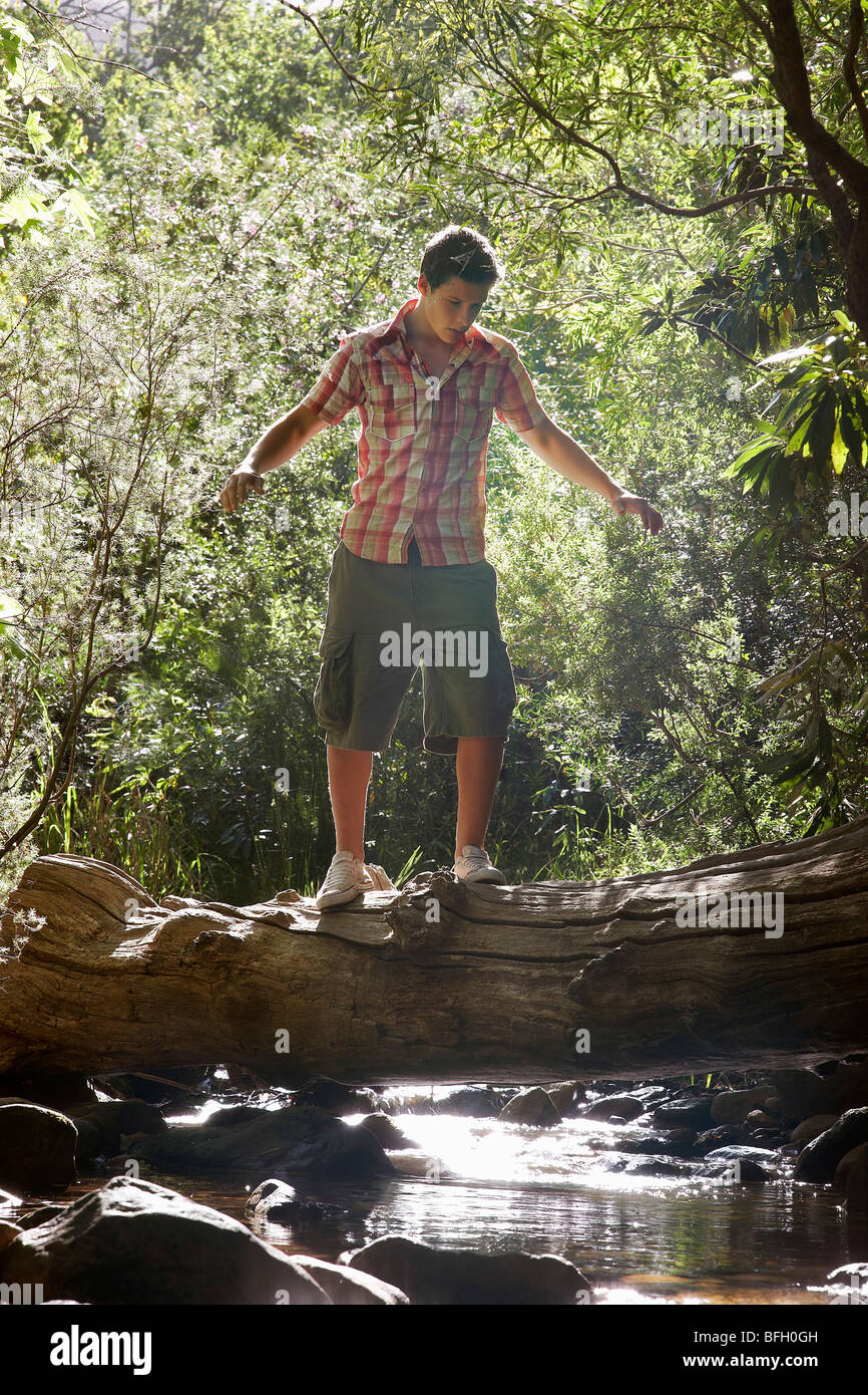 Teenage boy (16-17 years) walking tree trunk above stream Stock Photo