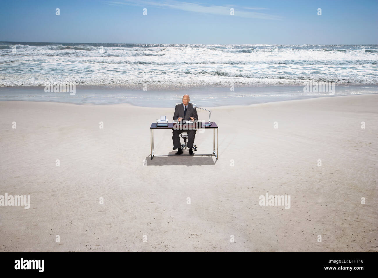 Senior business man sitting at office desk on beach, elevated view
