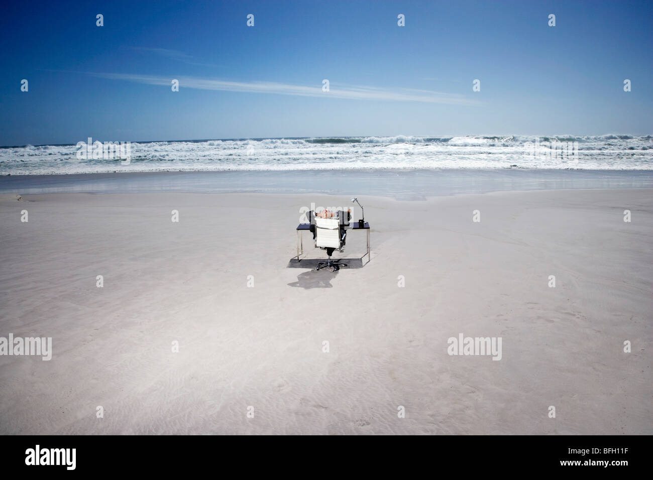 Senior business man sitting at office desk on beach, elevated view