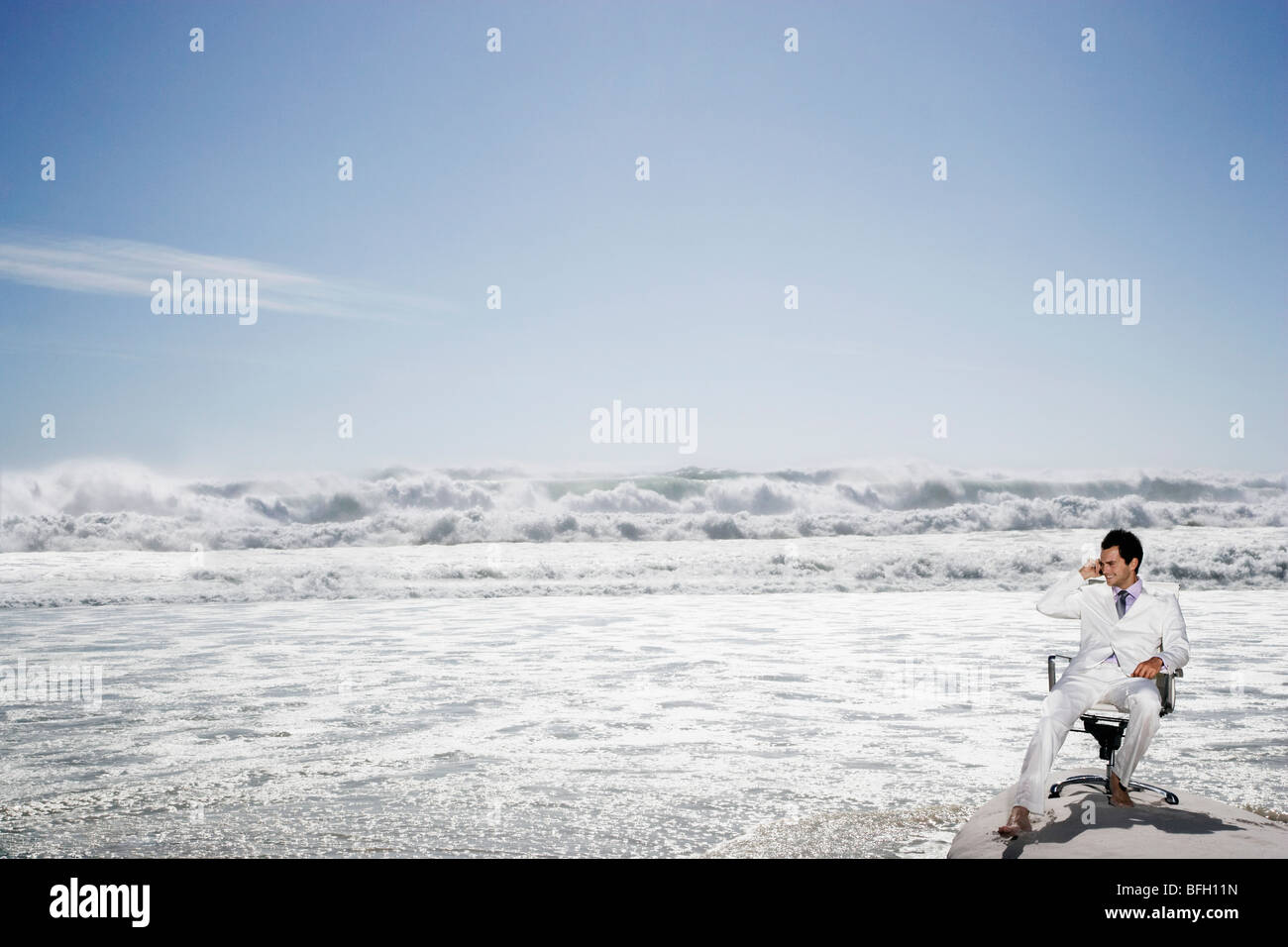 Man using mobile phone sitting on office chair on beach Stock Photo