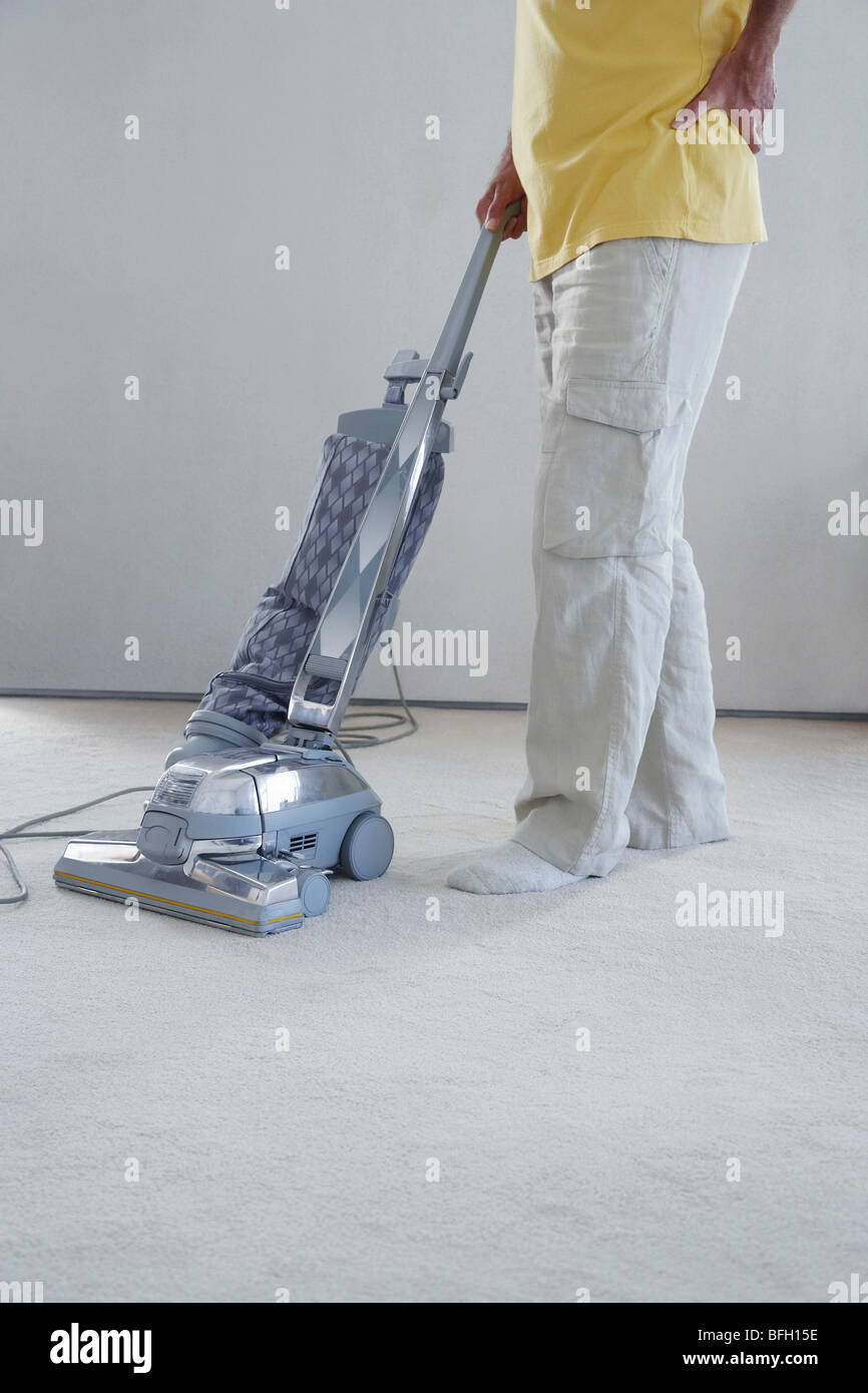 Mature man vacuuming carpet, holding lower back in pain, low section