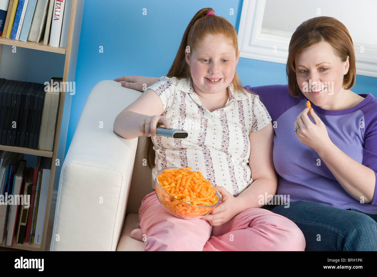 Overweight girl and mother watching television on sofa Stock Photo