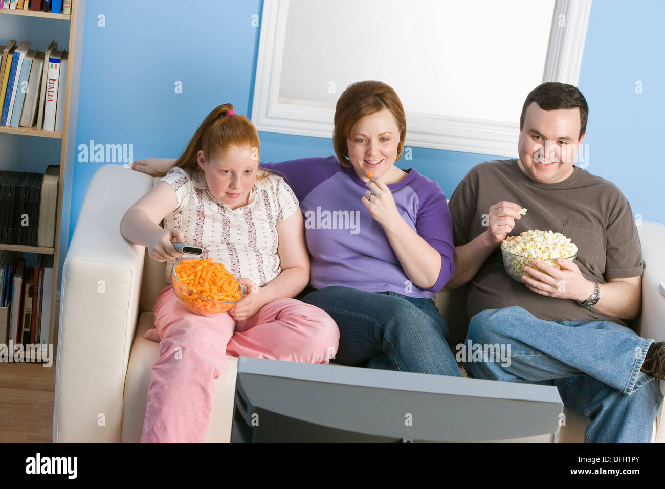 Overweight family watching television on sofa Stock Photo