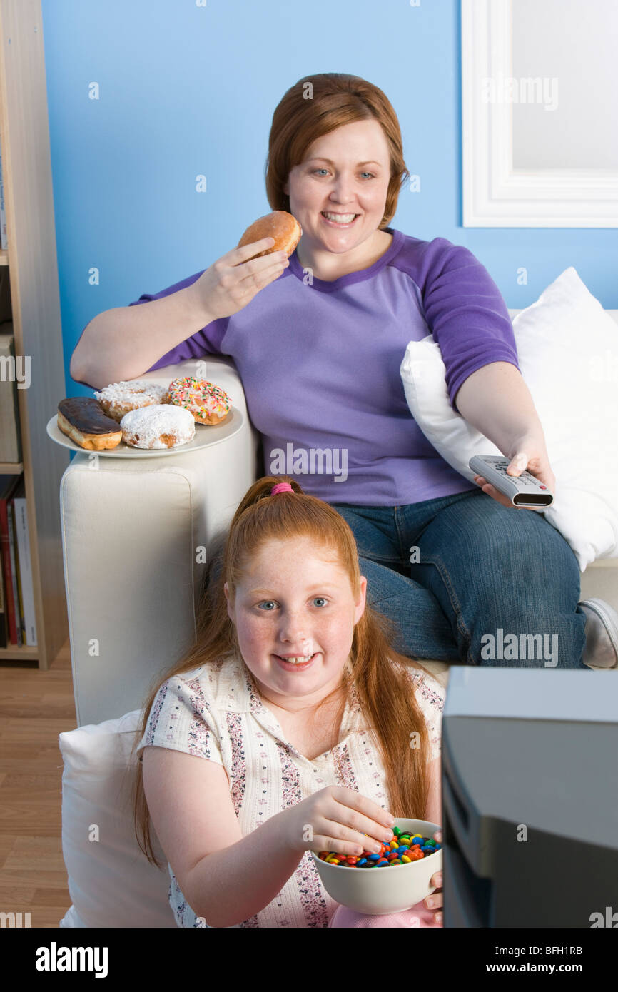 Overweight girl and mother watching television, eating Stock Photo