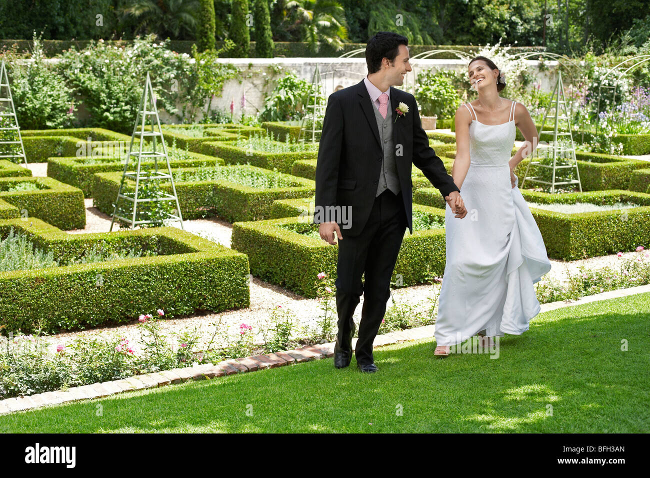 Bride and groom walking hand in hand in garden Stock Photo - Alamy