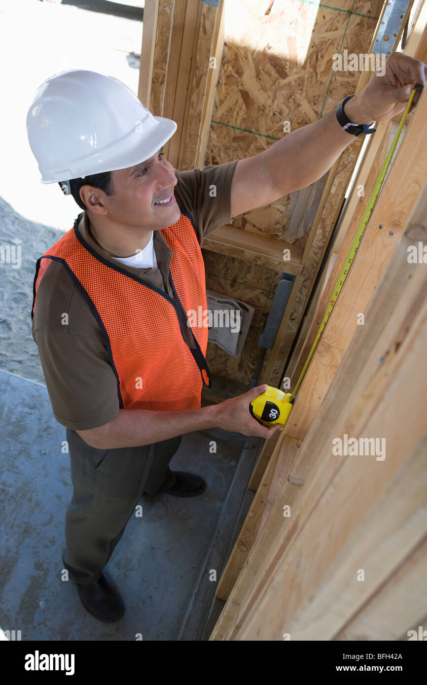 Construction worker measuring wall with measure taper inside half