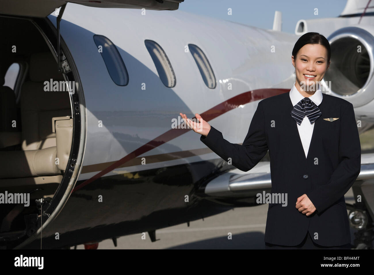 Female Asian mid-adult flight attendant in front of private jet. Stock Photo
