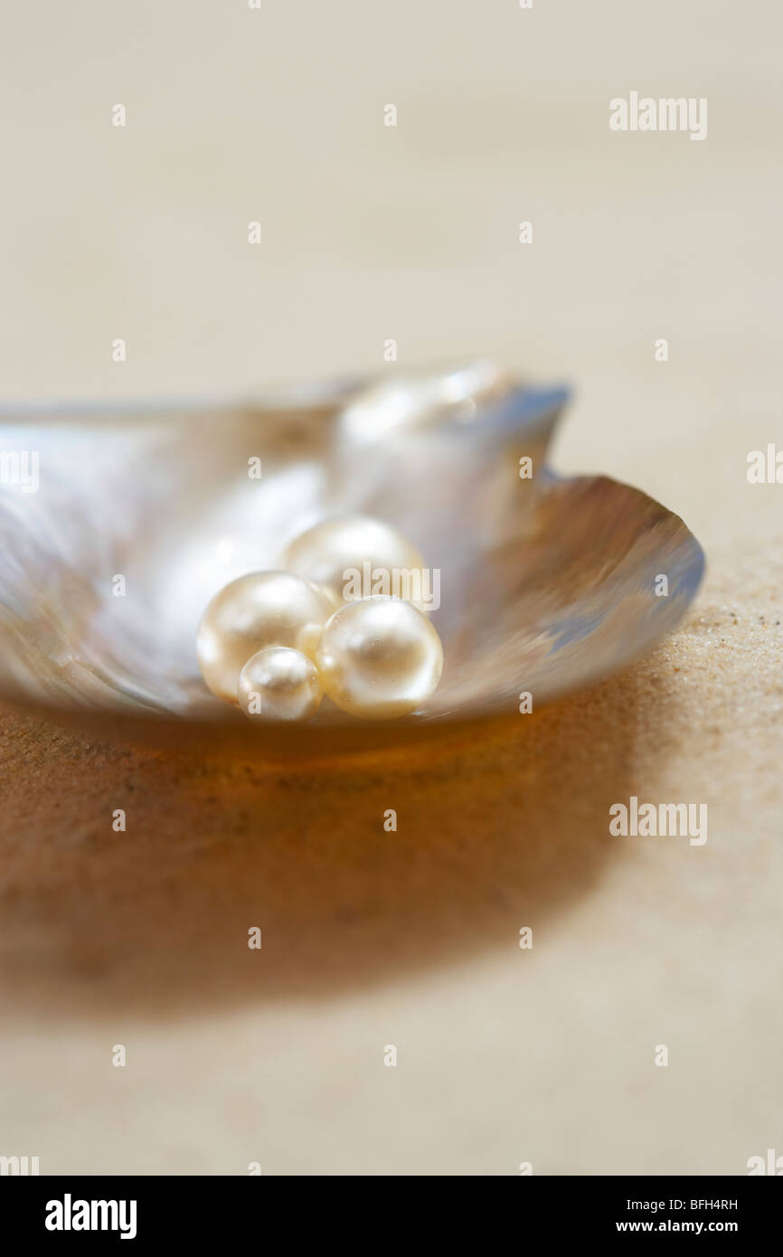 Four pearls in open oyster shell on beach, close up Stock Photo