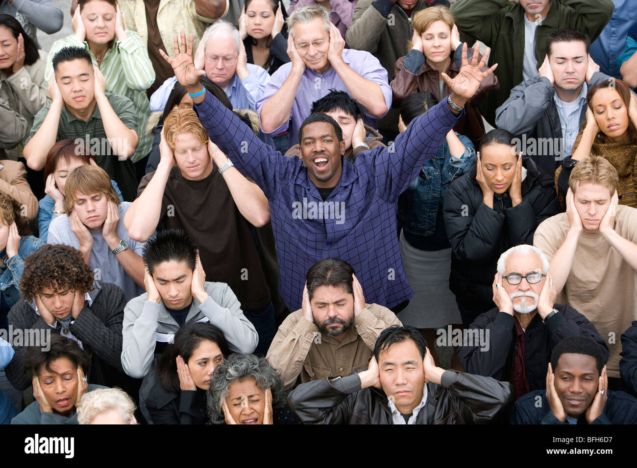 Man celebrating among crowd covering ears Stock Photo