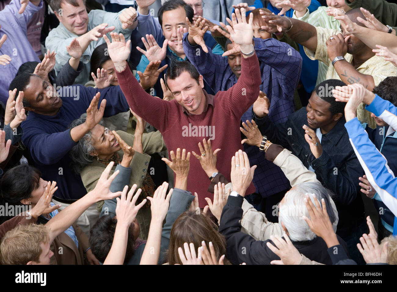 Crowd with arms raised surrounding man Stock Photo