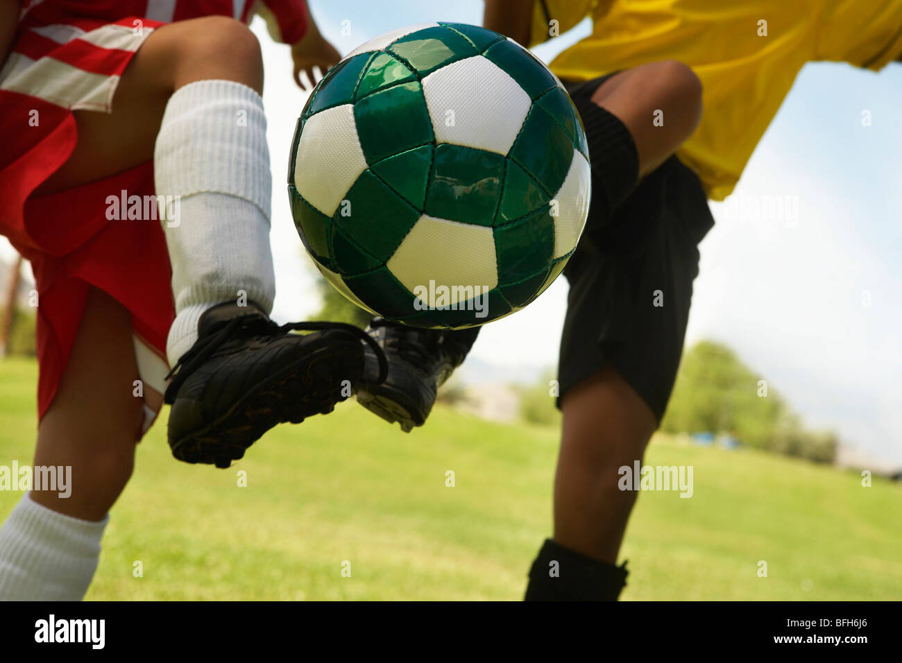 Two little league players (7-9 years) kicking ball mid air, mid section, close up Stock Photo