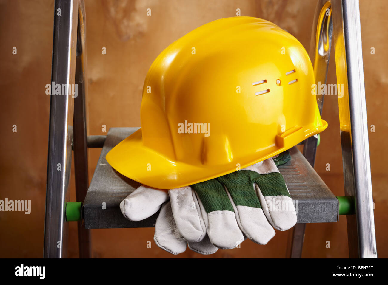 yellow helmet and working gloves on stepladder, selective focus on nearest parts Stock Photo