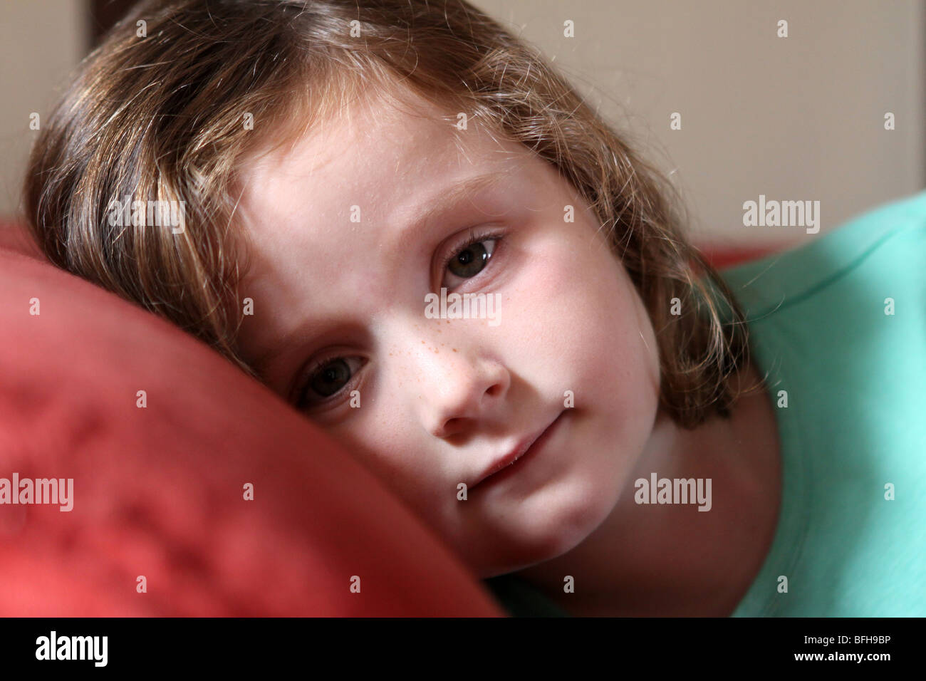 female child lying on red sofa looking towards camera with serious thoughtful pose Stock Photo