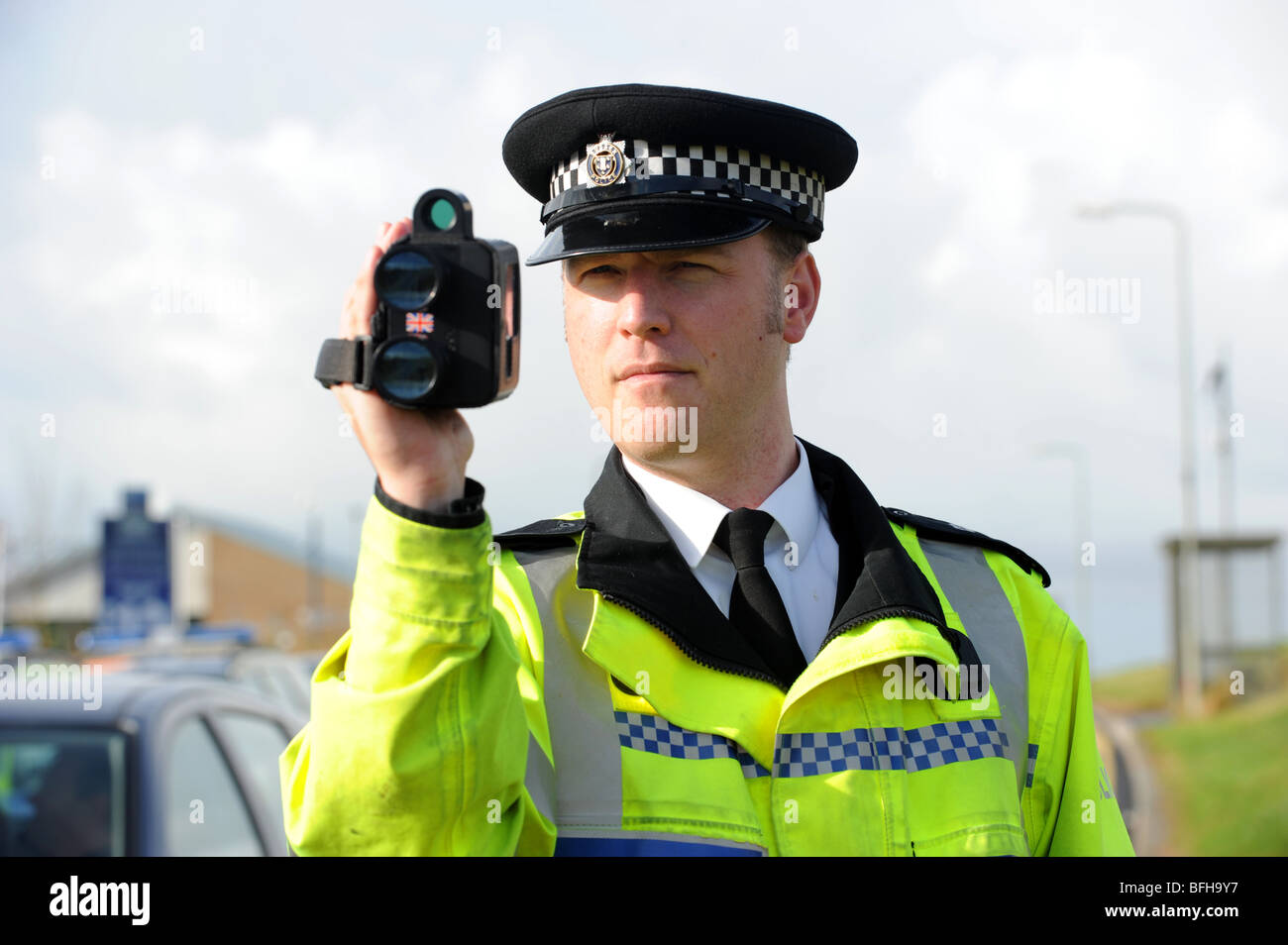 A policeman from Sussex police uses a hand held speed camera at the side of a busy road Stock Photo