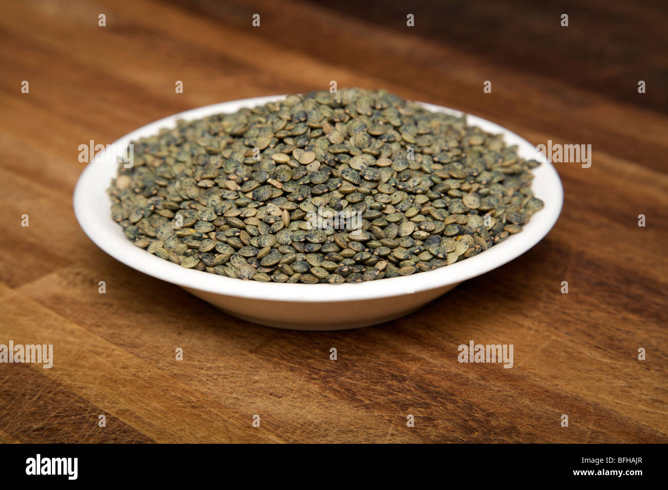 Cooking Ingredient Lentil Seeds in a white bowl on a kitchen work surface. Stock Photo