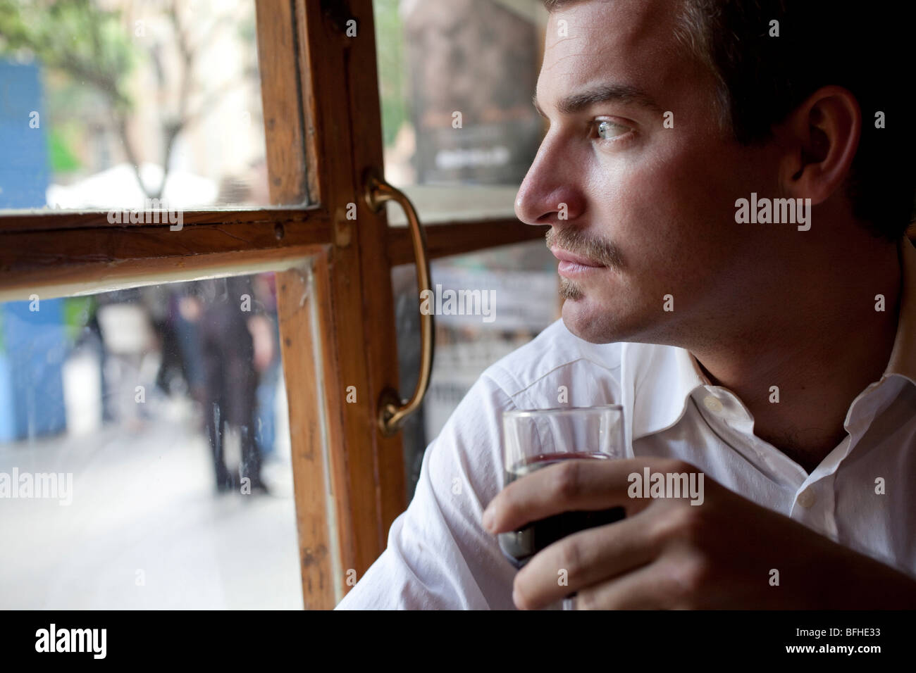 young man looking out the window holding a glass of wine Stock Photo