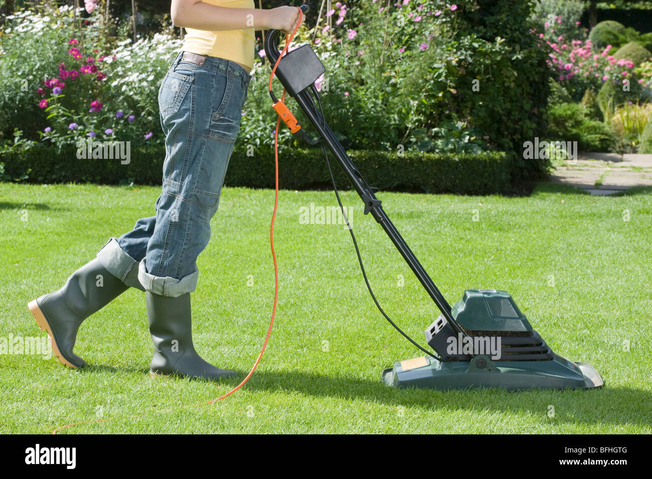 Woman Mowing Lawn With electric Lawn Mower Stock Photo
