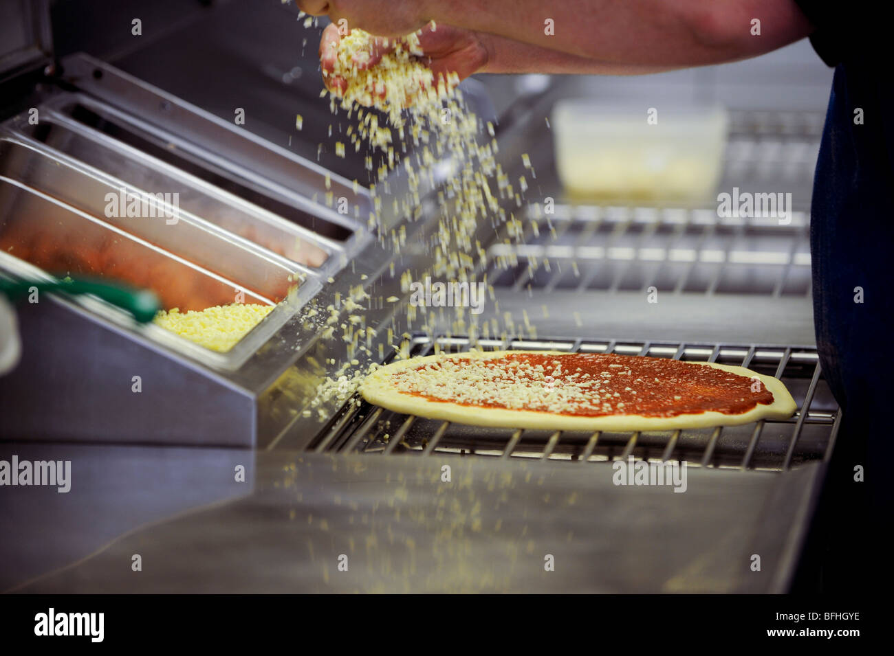 Cheese topping being added to a fresh pizza at a takeaway pizza store