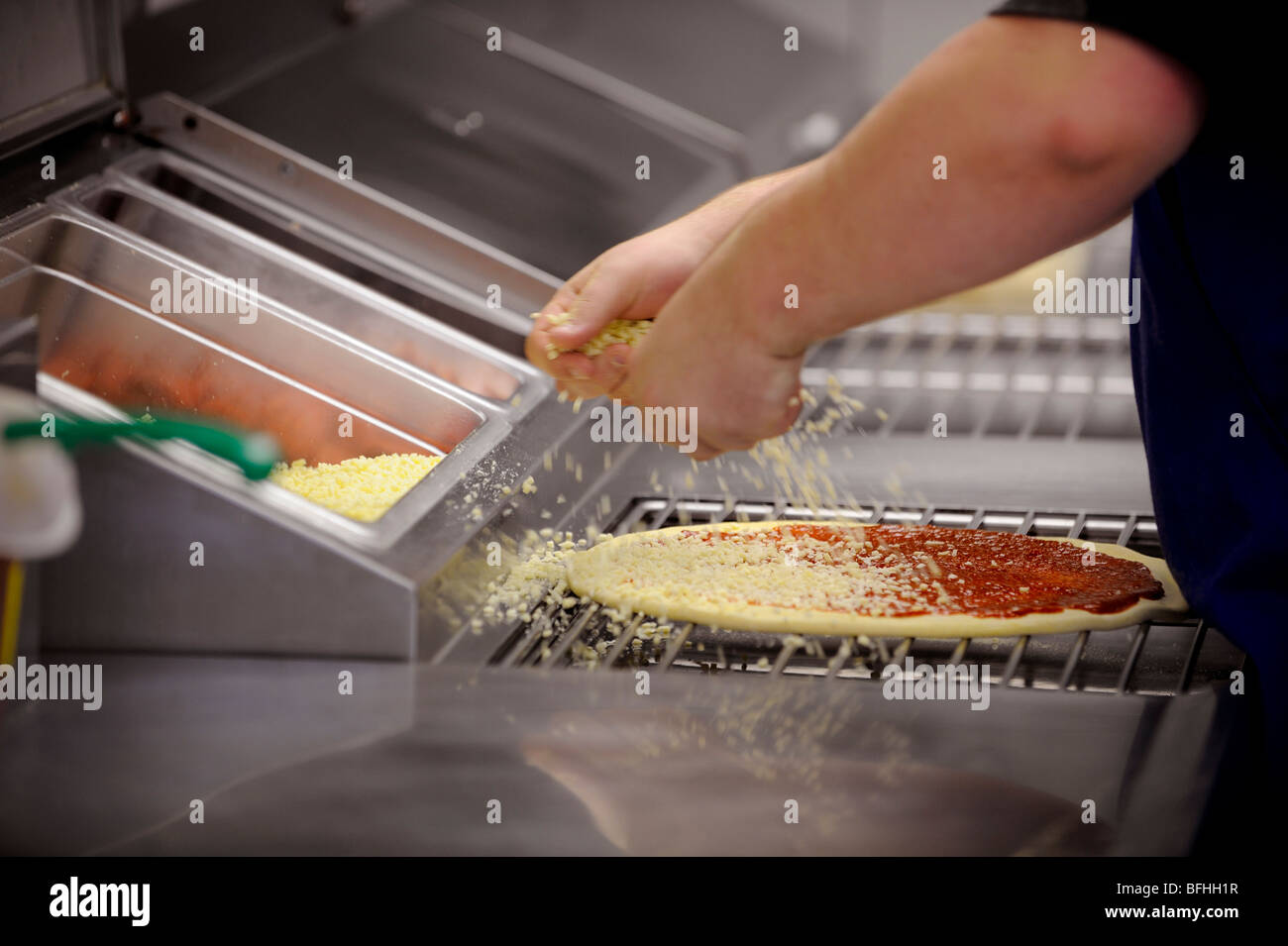 Cheese topping being added to a fresh pizza at a takeaway pizza store. Stock Photo