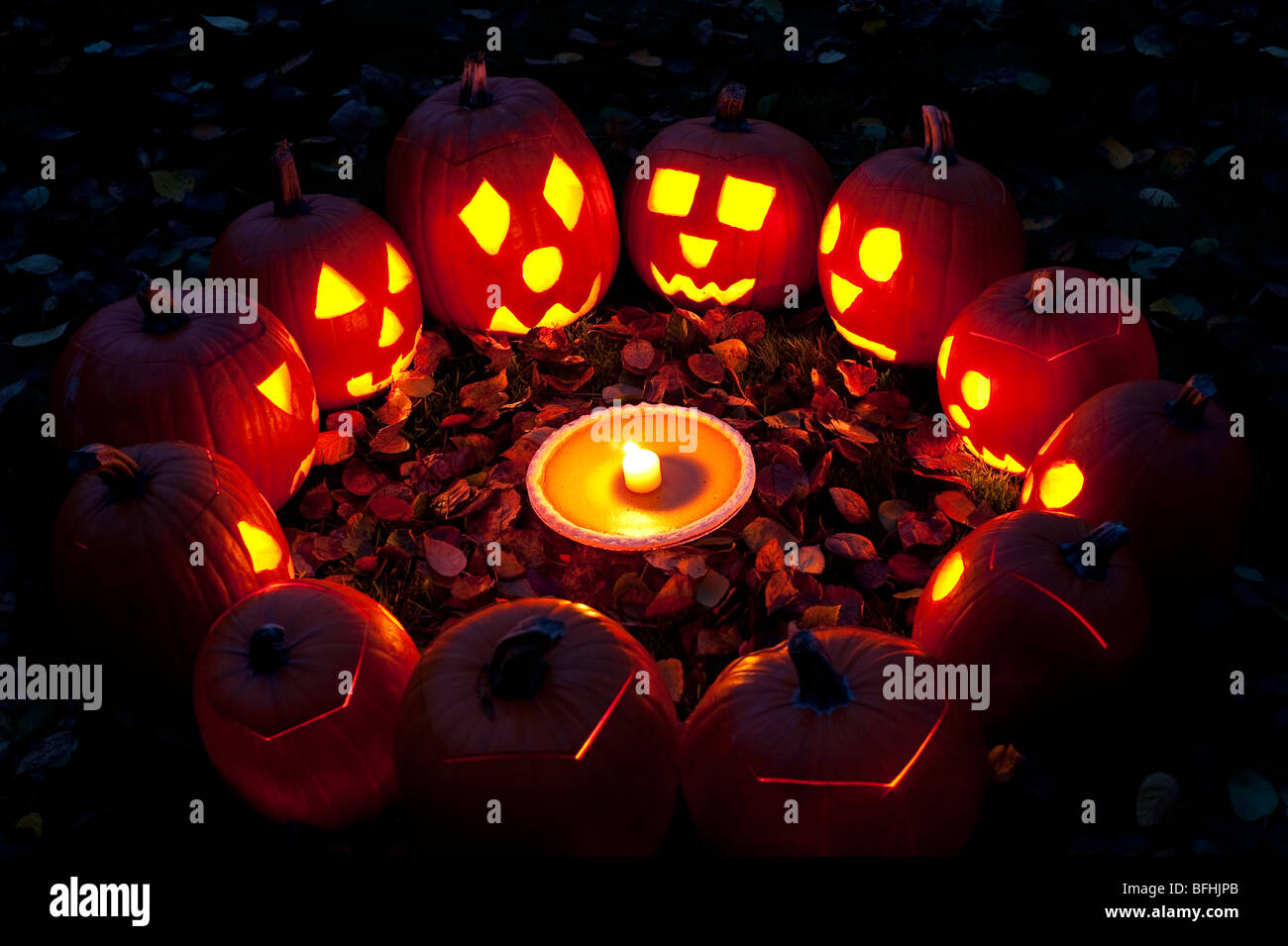 Carved pumpkins in a circle at twilight around a pumpkin pie on Halloween night Stock Photo