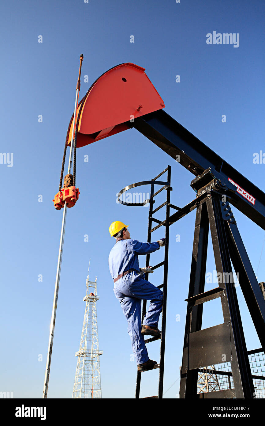 Worker climbing pump jack with oil drilling rig in background at Canadian Petroleum Discover Museum in Devon, Alberta, Canada. Stock Photo