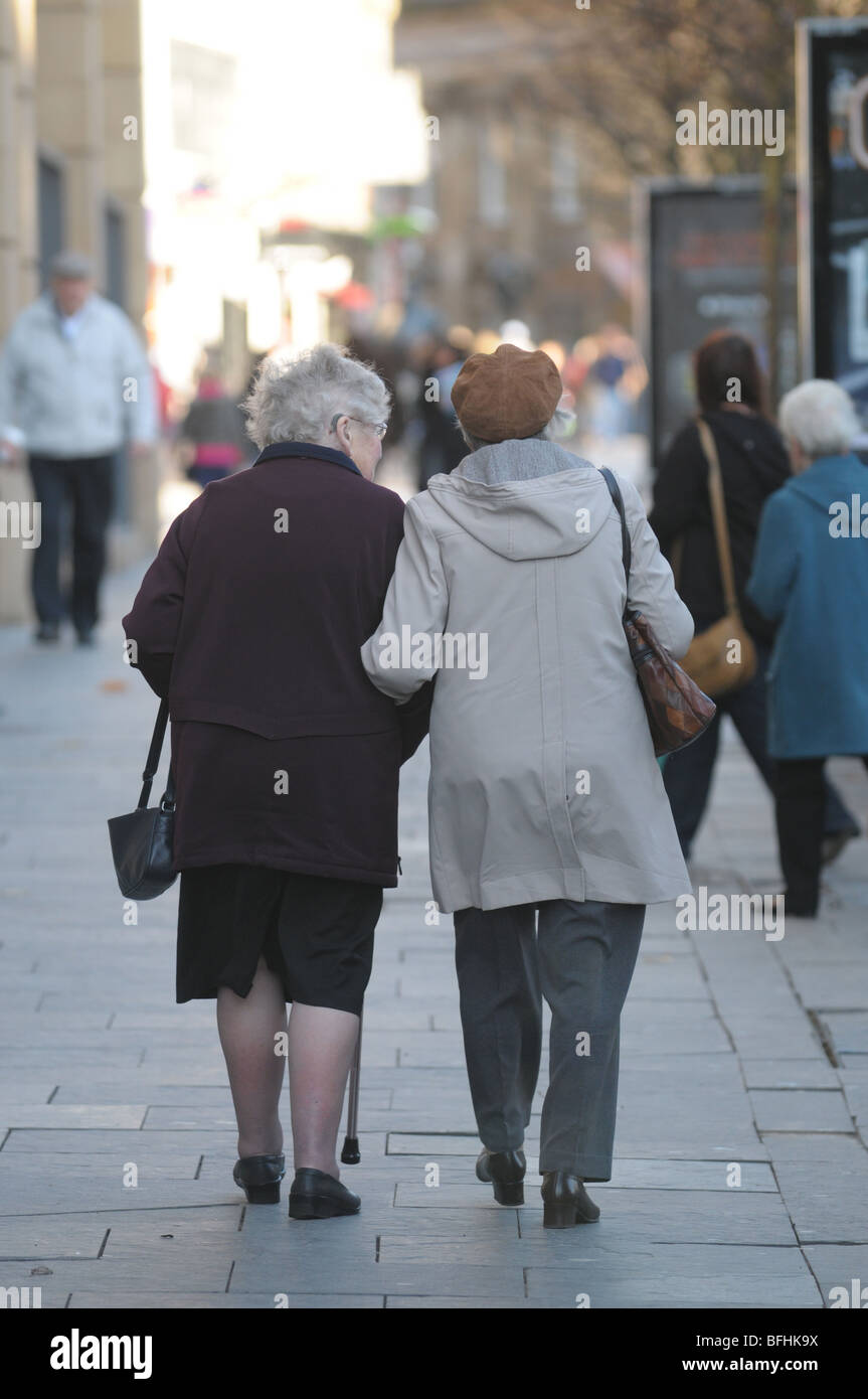 Two Elderly Ladies Holding Arms And Walking Along The Pavement Stock Photo Alamy