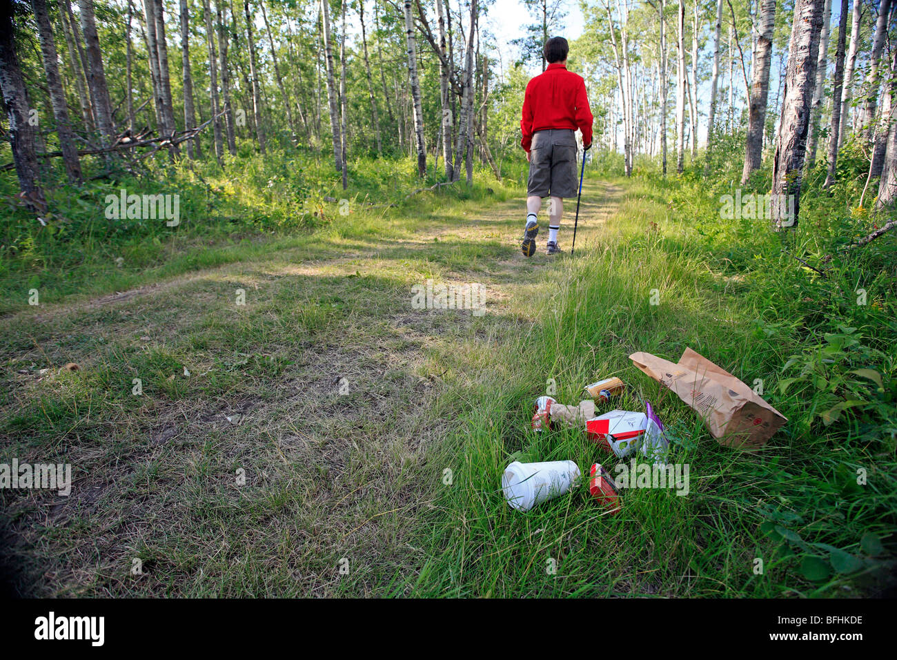 Middle age male hiking on forest trail with garbage on the ground. Stock Photo