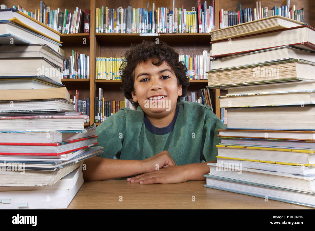 School boy sitting at desk with books in library, portrait Stock Photo ...