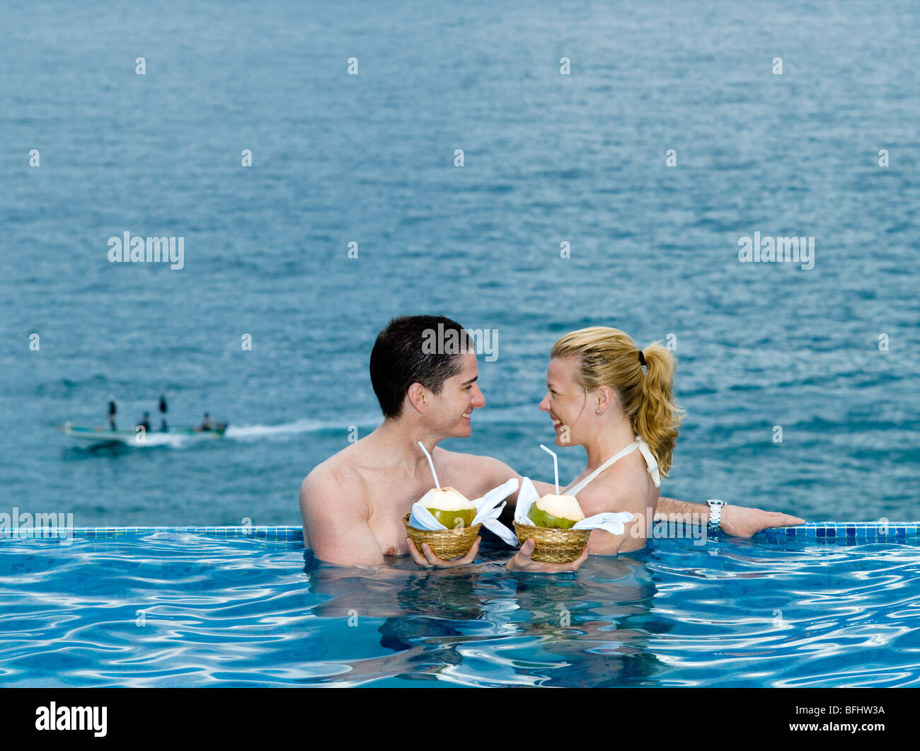 beautiful caucasian couple enjoying their vacation in a swimming pool by the seaside drinking coconut milk Stock Photo