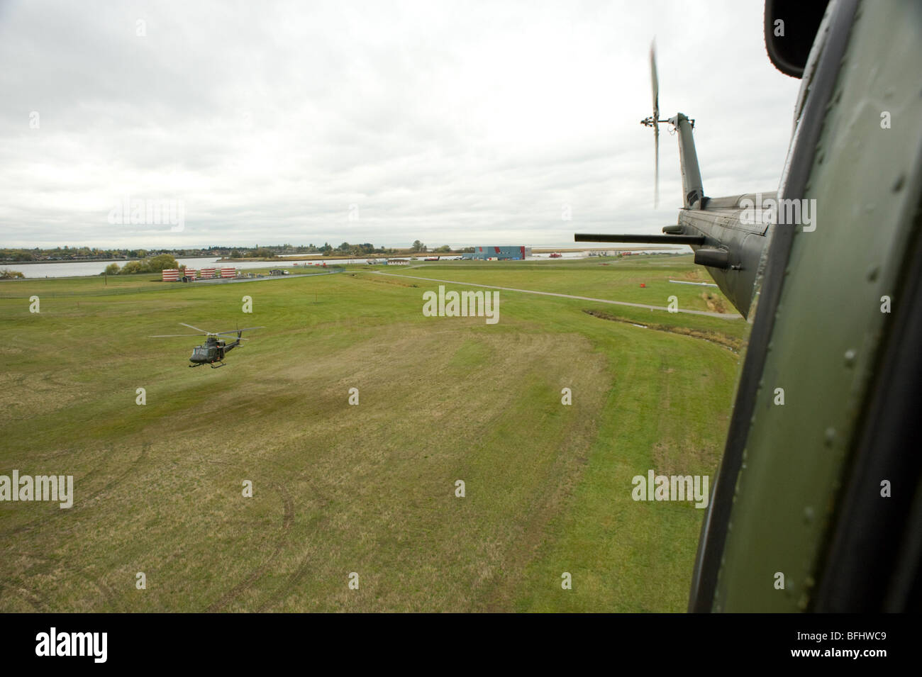 two military bell helicopters taking off from grass pad Stock Photo