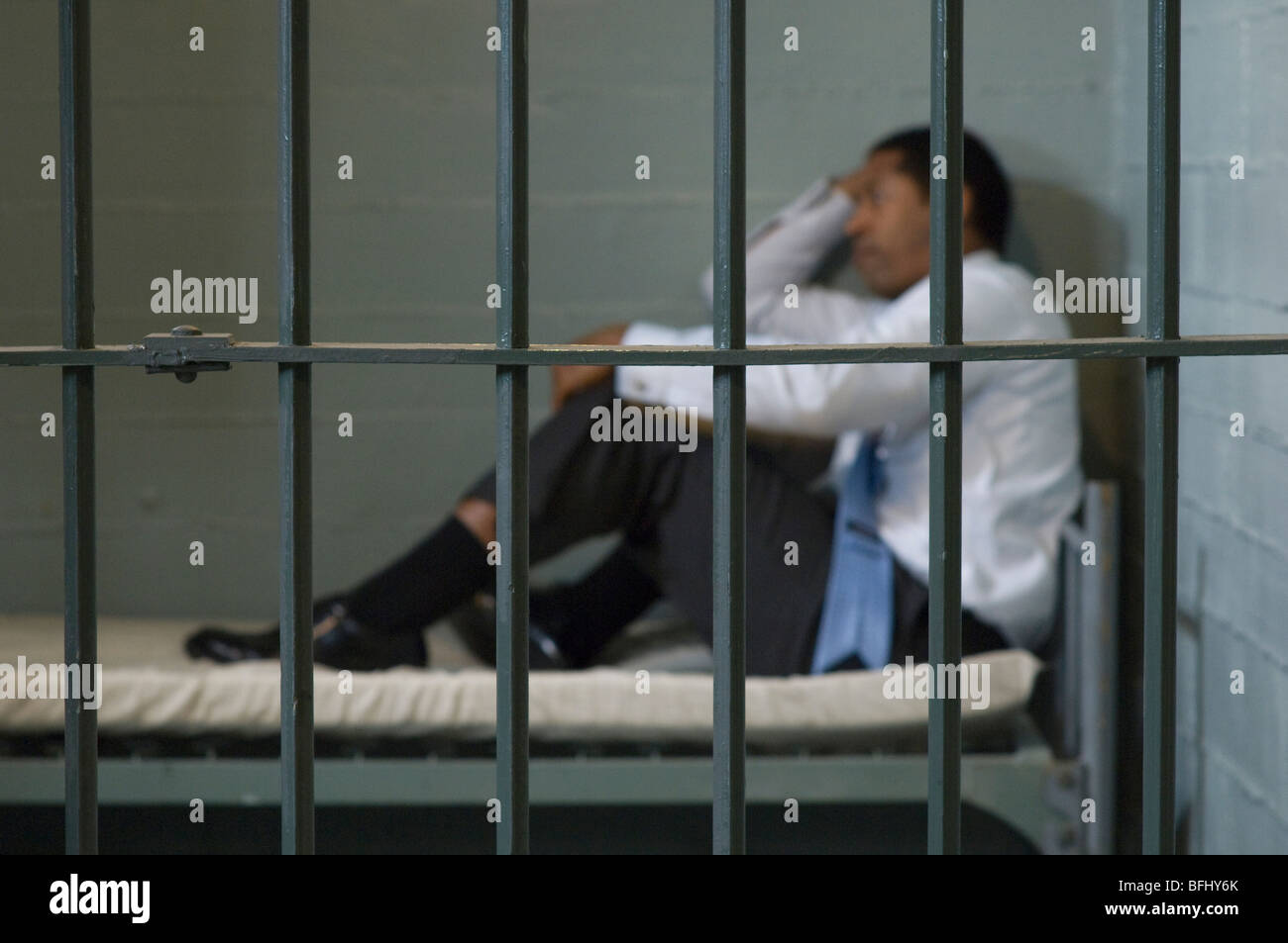Mature man sitting on bed in prison cell Stock Photo
