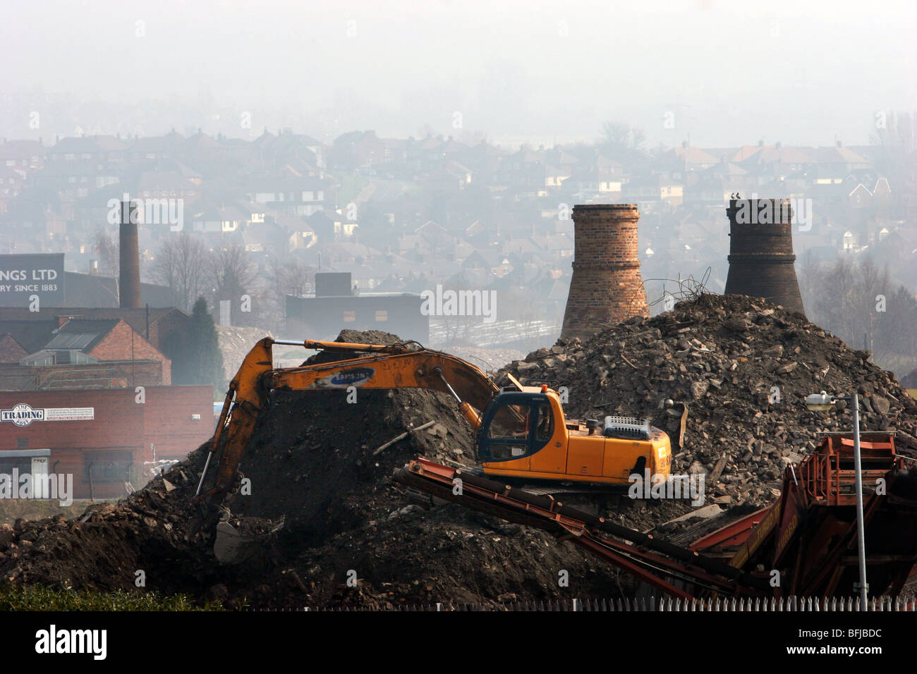 A JCB style digger clearing rubble in Stoke on Trent, Staffordshire with a city skyline including pot banks in the background Stock Photo
