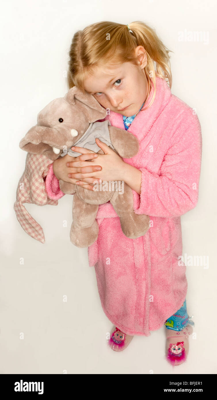 Little, caucasian girl in her pyjamas, slippers and dressing gown  ready for bed cuddling her toy Stock Photo