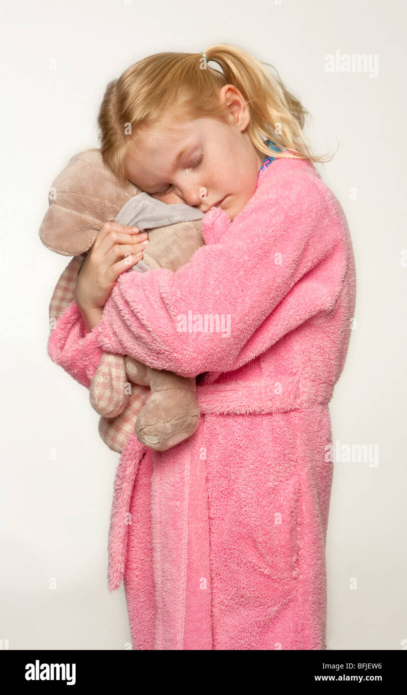 Little, caucasian girl in her pyjamas, slippers and dressing gown  ready for bed cuddling her toy Stock Photo