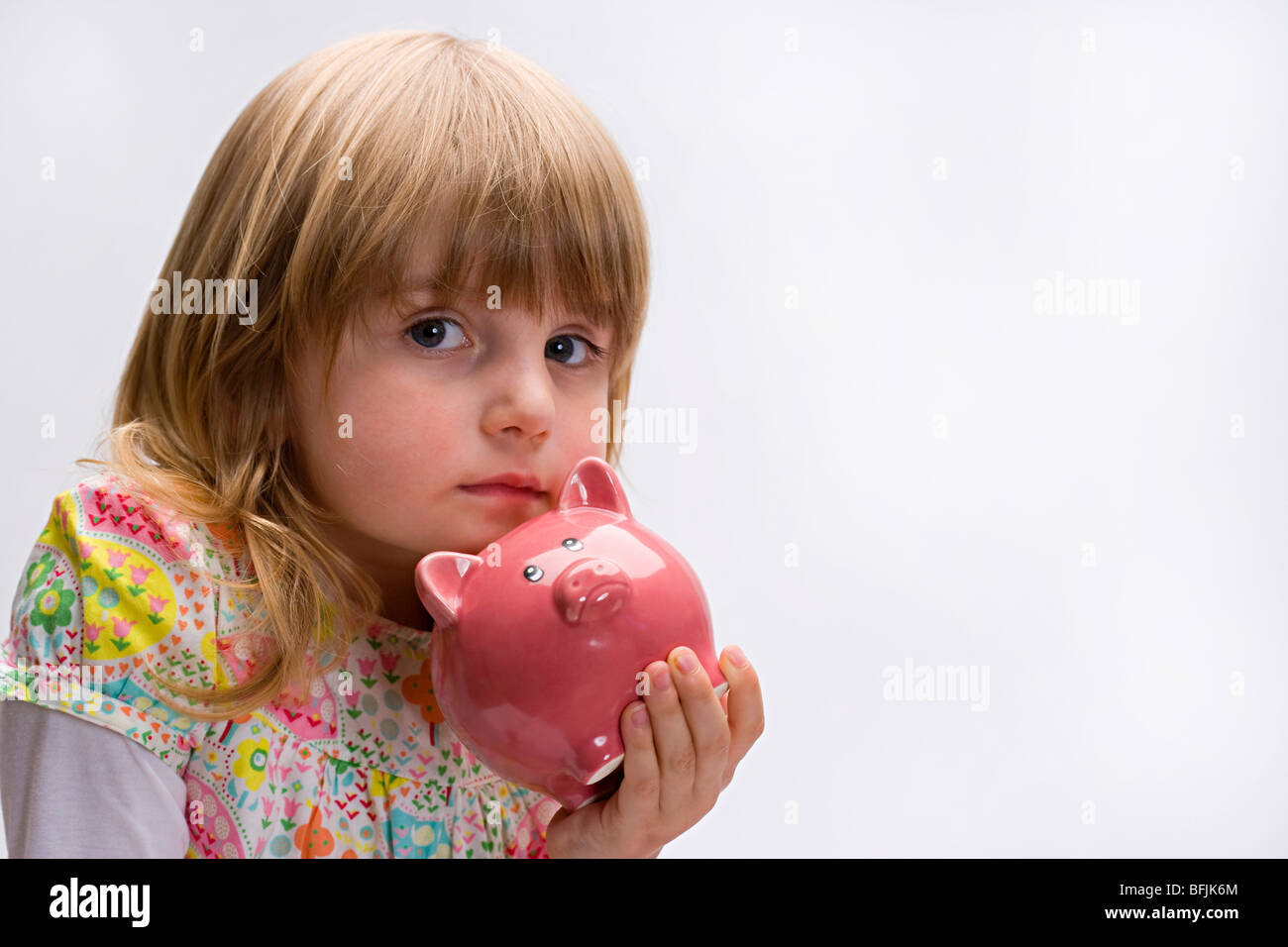 Young girl holding a pink piggy bank close to her face looking like she's lost her savings Stock Photo