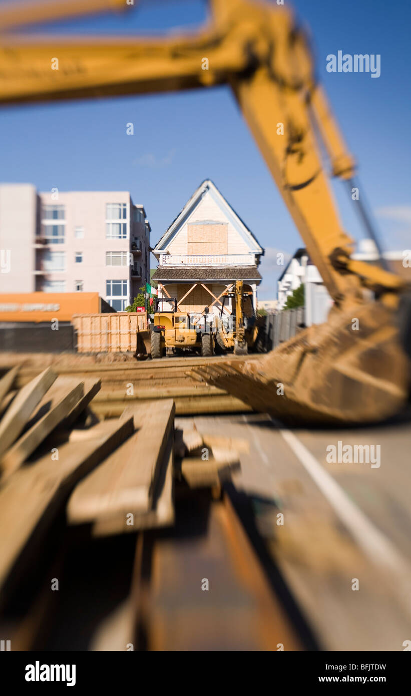 An artistic photo of a backhoe, seen in a construction site in an urban setting, with planks of wood in the foreground. Stock Photo