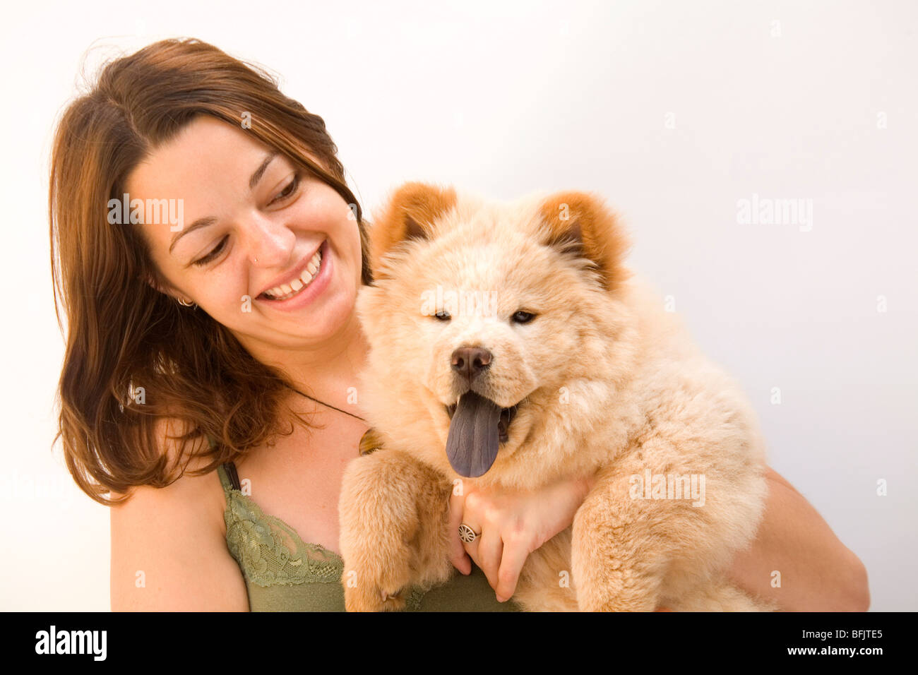 A young Caucasian woman smiles as she holds her 8-week-old chow chow puppy. Stock Photo