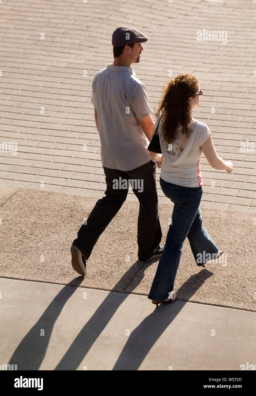 A stylish young couple walk together in the summer sunshine, the sun casting strong shadows behind them. Stock Photo