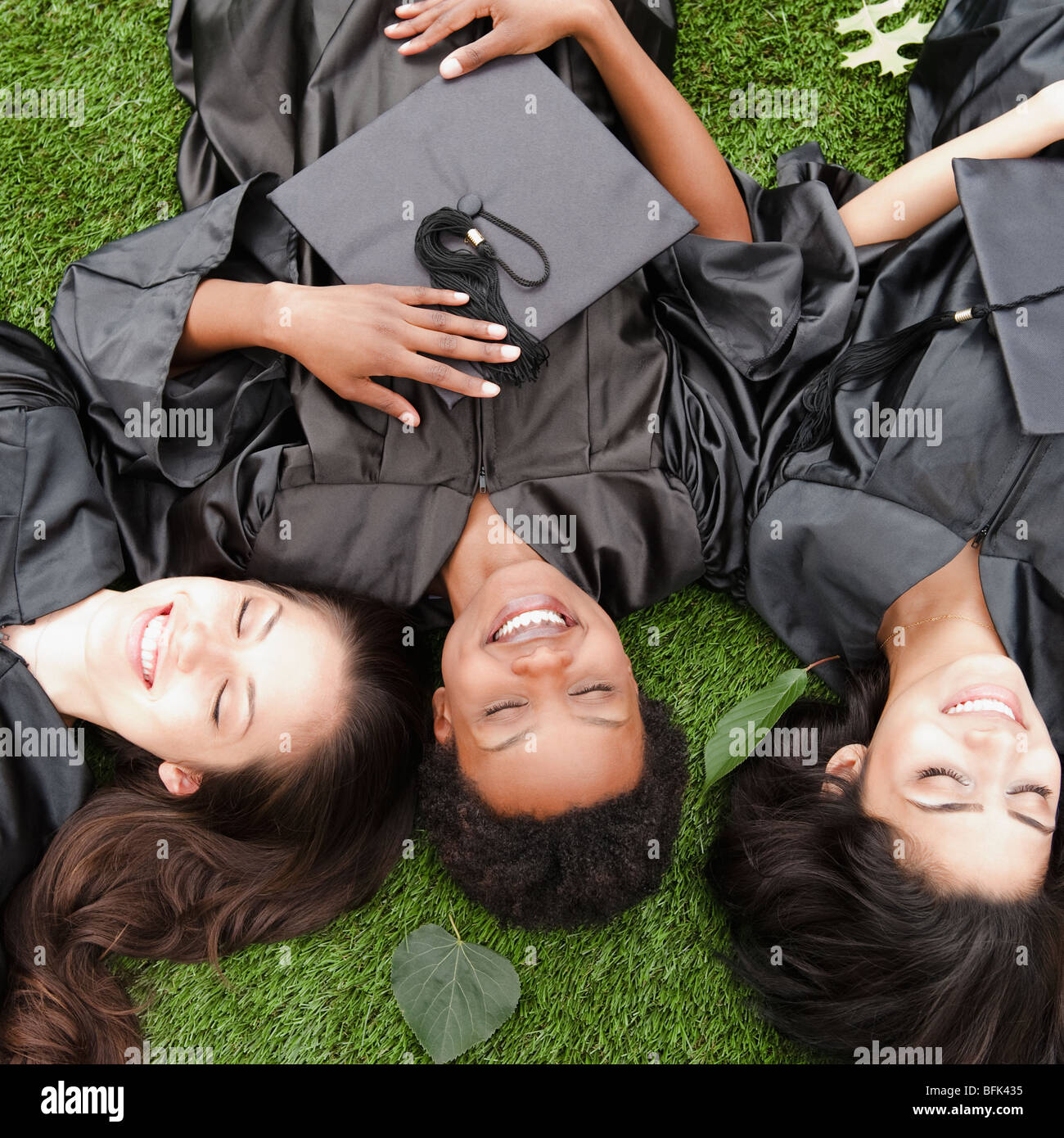 Friends in caps and gowns laying in grass Stock Photo