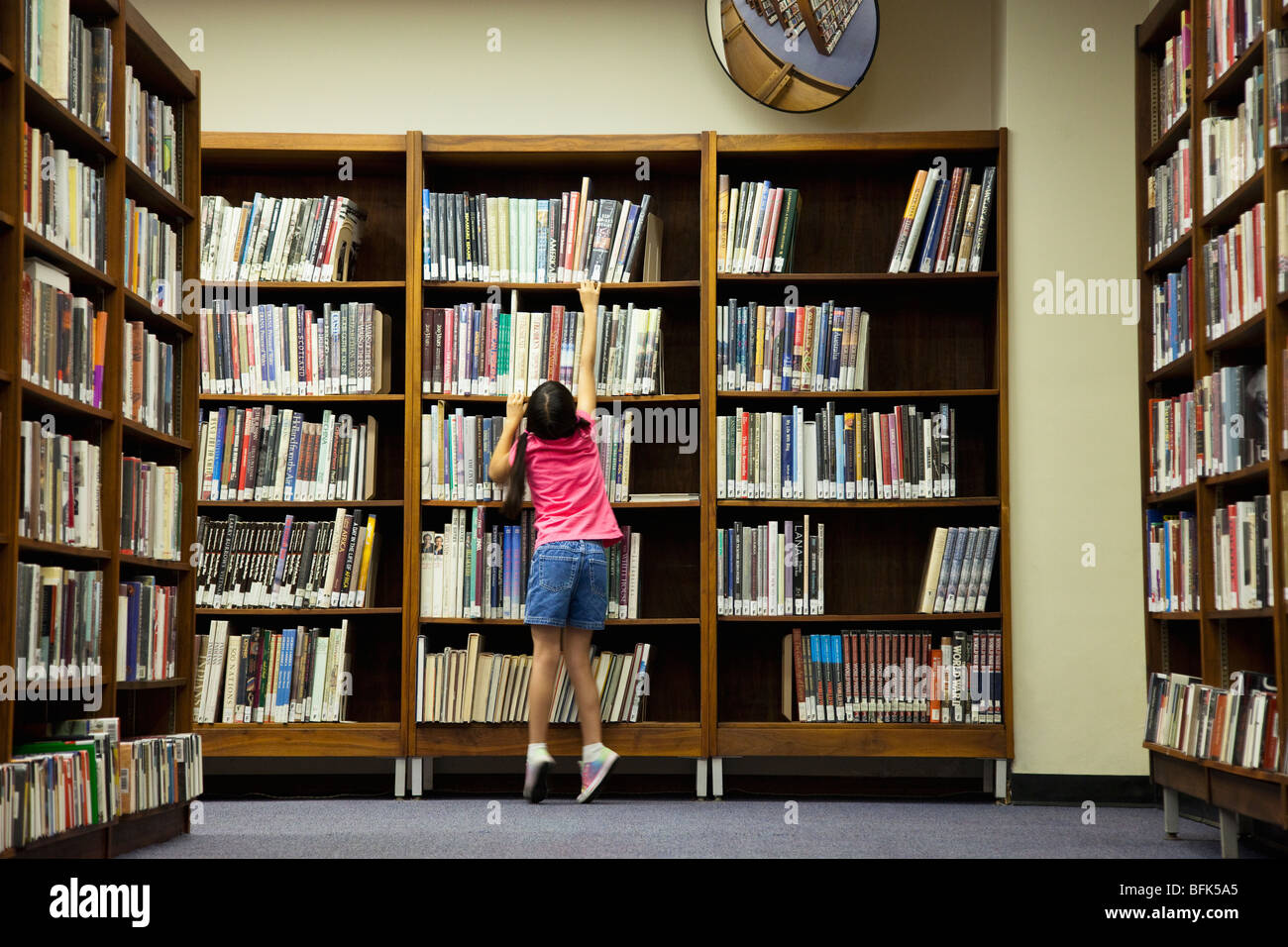 Girl reaching for book on library shelf Stock Photo Alamy
