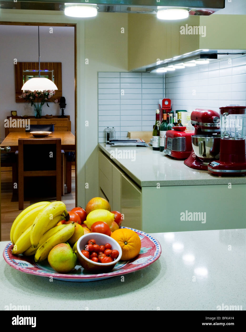 Bowl of fruit and tomatoes on a modern kitchen worktop with view into dining room Stock Photo