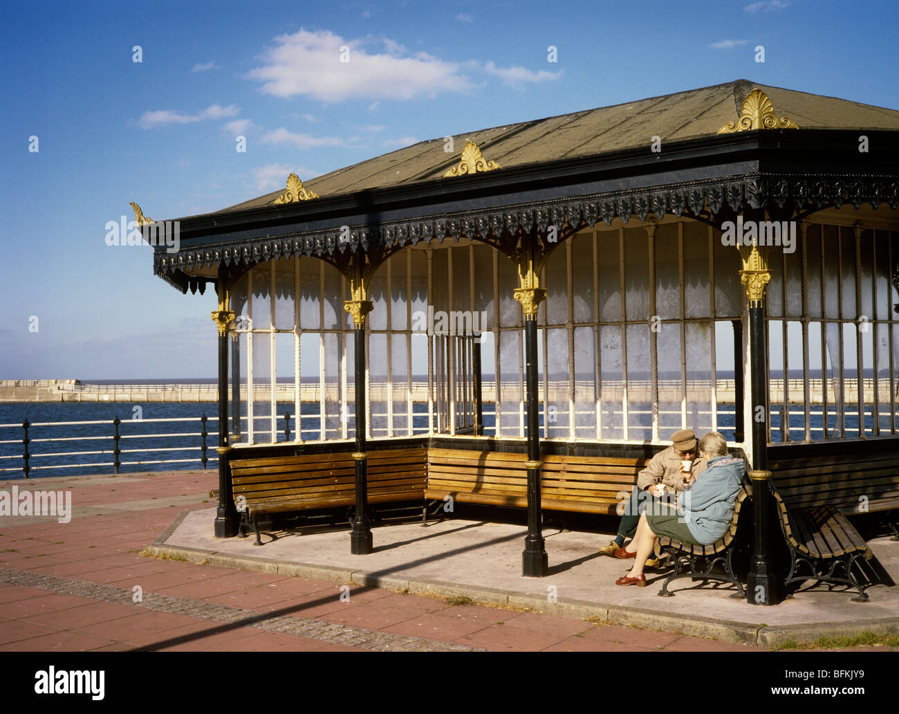 UK, England, Wirral, New Brighton, elderly couple sat in seafront shelter sheltering from sea breeze Stock Photo